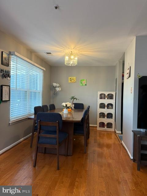 dining room featuring a notable chandelier, wood-type flooring, visible vents, and baseboards