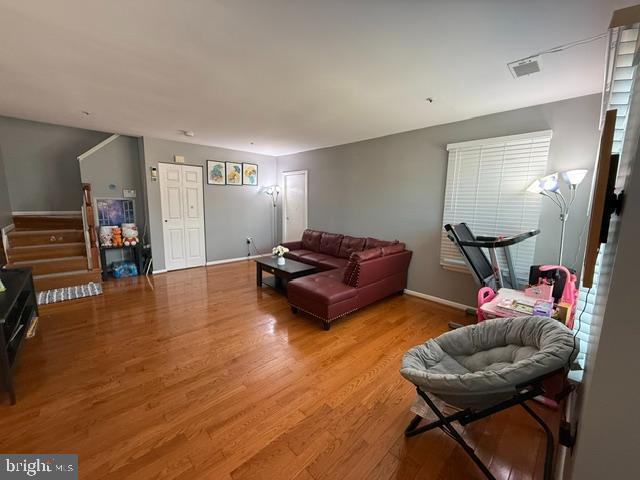 living area with baseboards, visible vents, stairway, and wood finished floors