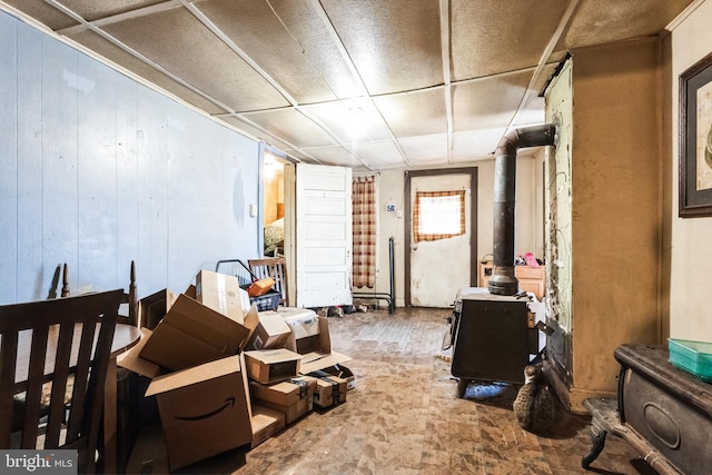 finished basement with a wood stove, wooden walls, and a drop ceiling