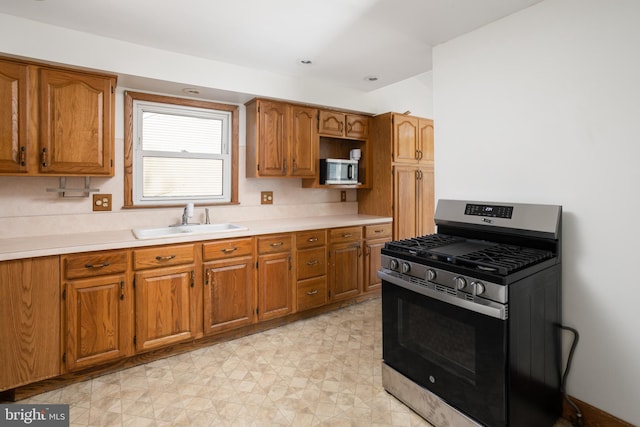 kitchen featuring light floors, light countertops, brown cabinetry, stainless steel appliances, and a sink