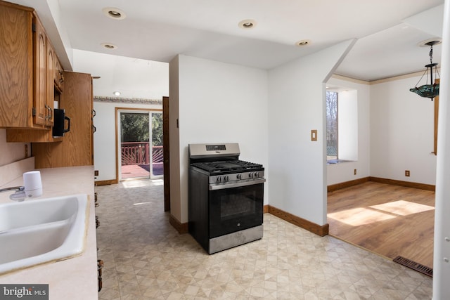 kitchen with brown cabinetry, gas stove, visible vents, a sink, and light countertops