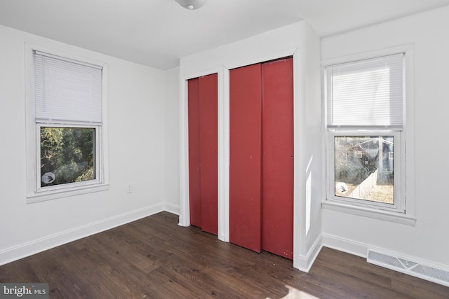 unfurnished bedroom with wood finished floors, visible vents, two closets, and baseboards