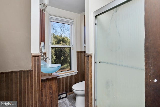 bathroom featuring wooden walls, a sink, an enclosed shower, wainscoting, and toilet