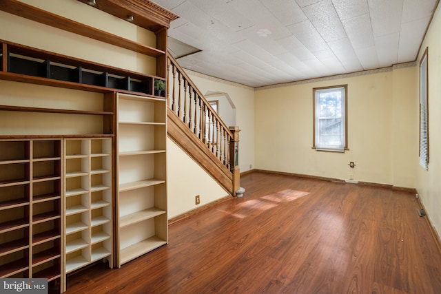 unfurnished living room featuring stairway, wood finished floors, baseboards, and ornamental molding