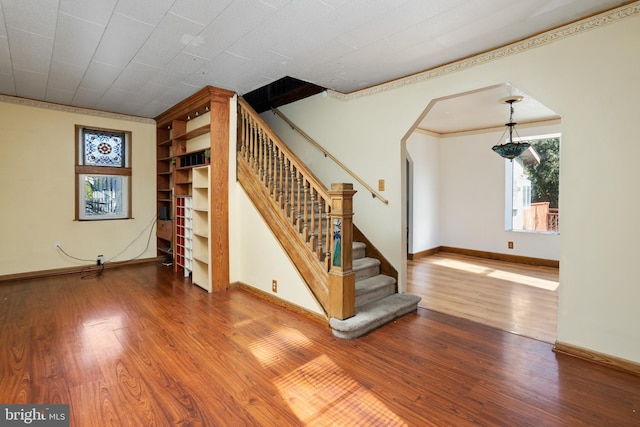 interior space with crown molding, baseboards, stairs, wood finished floors, and arched walkways