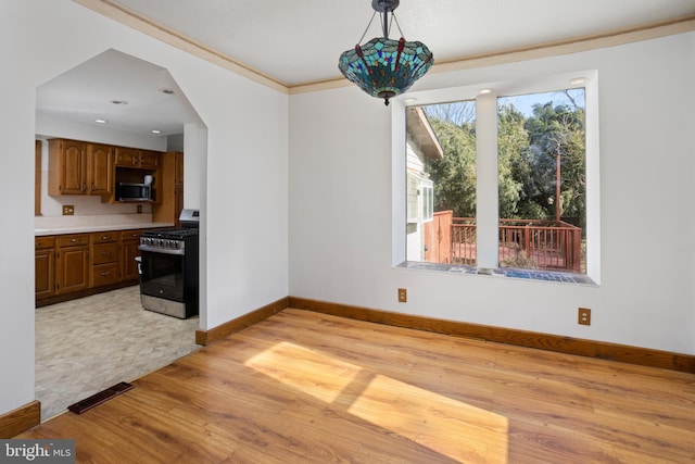 dining space featuring baseboards, visible vents, light wood finished floors, arched walkways, and crown molding