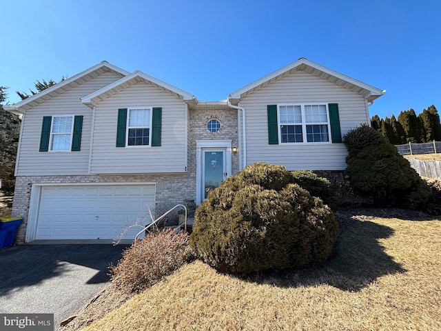 split foyer home with a garage, brick siding, driveway, and fence