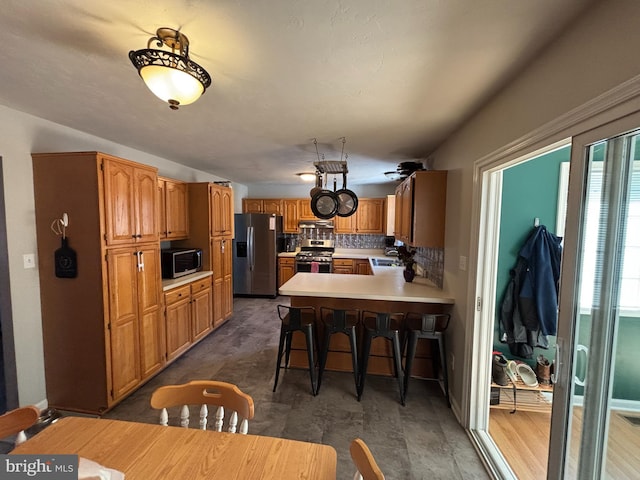 kitchen with tasteful backsplash, a peninsula, stainless steel appliances, light countertops, and a kitchen bar