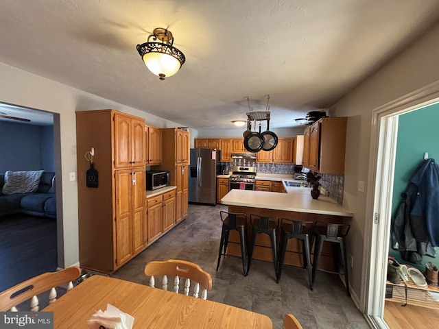 kitchen with a peninsula, a sink, stainless steel appliances, light countertops, and backsplash