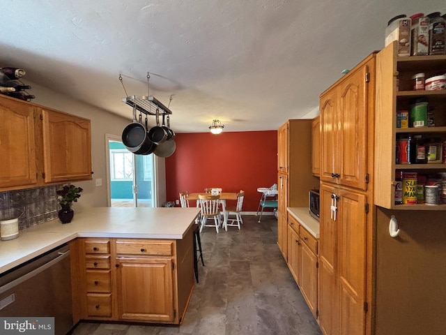 kitchen featuring a peninsula, light countertops, appliances with stainless steel finishes, backsplash, and brown cabinetry