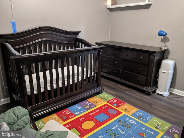 bedroom with a nursery area, baseboards, and wood finished floors