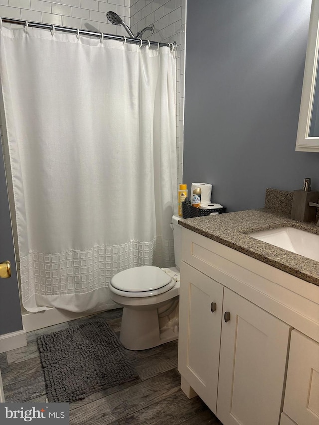 full bath with toilet, a shower with curtain, wood finished floors, and vanity