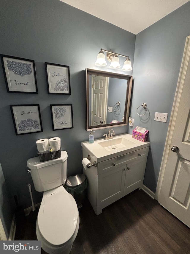 half bath with vanity, wood finished floors, toilet, and baseboards