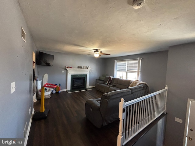 living room with baseboards, visible vents, a fireplace with raised hearth, wood finished floors, and a textured ceiling