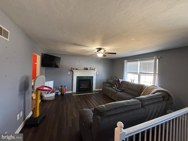 living room featuring visible vents, baseboards, a fireplace with raised hearth, wood finished floors, and a textured ceiling