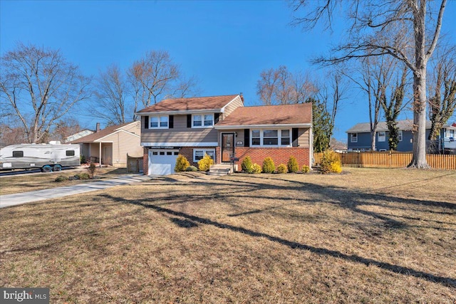 tri-level home with a front yard, fence, driveway, an attached garage, and brick siding