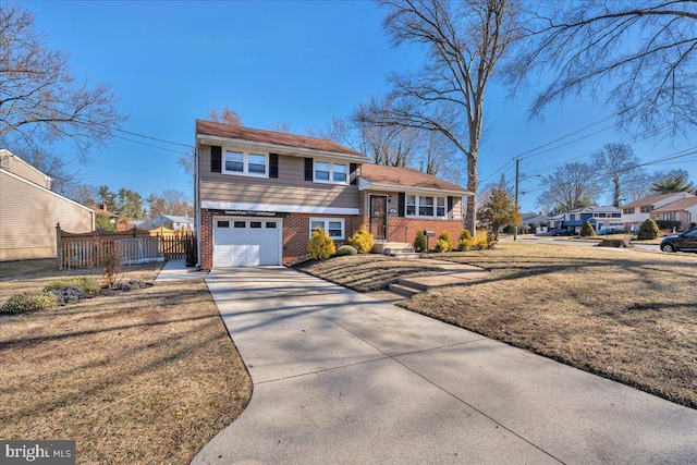 tri-level home featuring concrete driveway, fence, brick siding, and a front lawn