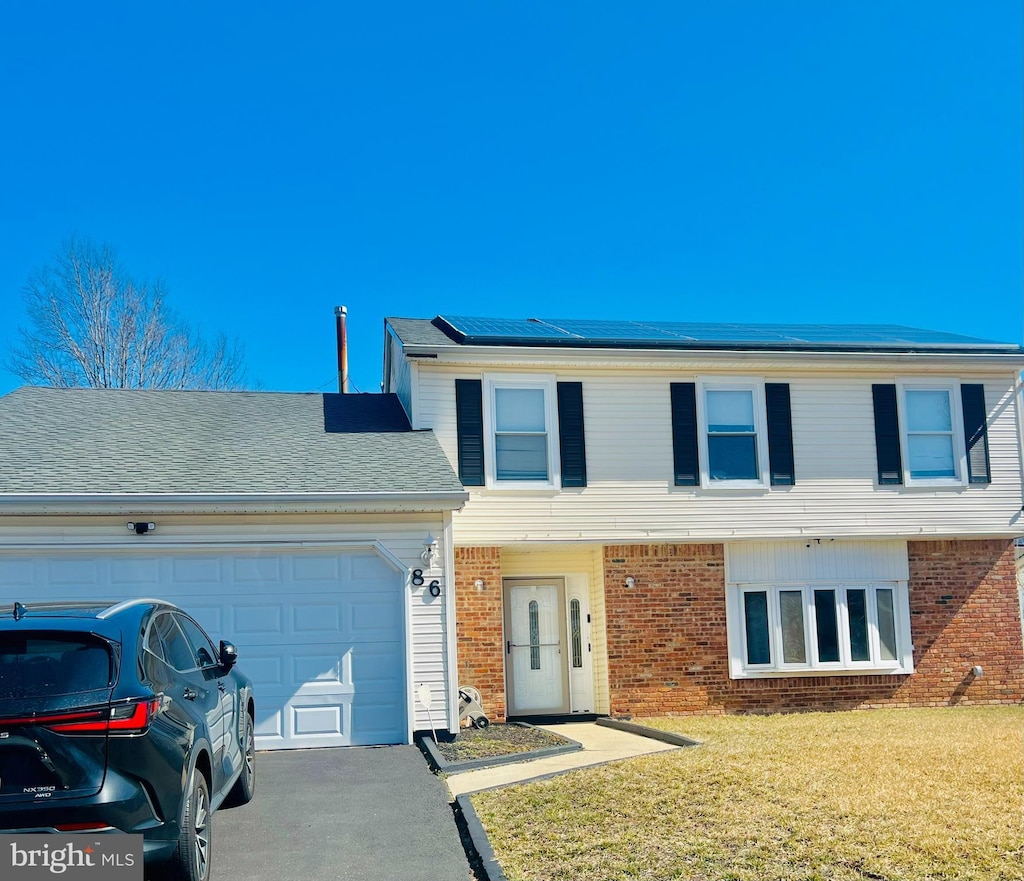 view of front of home featuring driveway, an attached garage, a front yard, brick siding, and solar panels