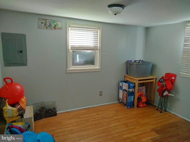 recreation room with electric panel, baseboards, and wood finished floors