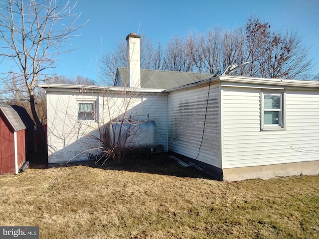 back of house with a lawn, a chimney, an outdoor structure, and heating fuel