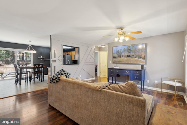 living room featuring visible vents, baseboards, ceiling fan, and dark wood-style flooring