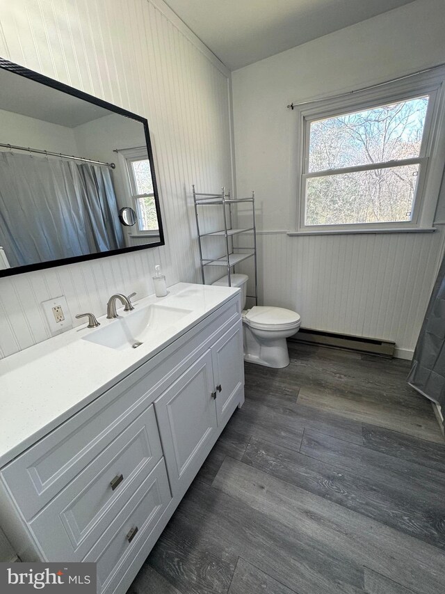 bathroom with vanity, wood finished floors, wainscoting, a baseboard heating unit, and toilet