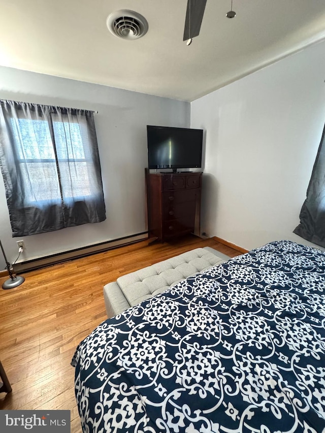 bedroom featuring visible vents, wood finished floors, baseboards, and a baseboard radiator