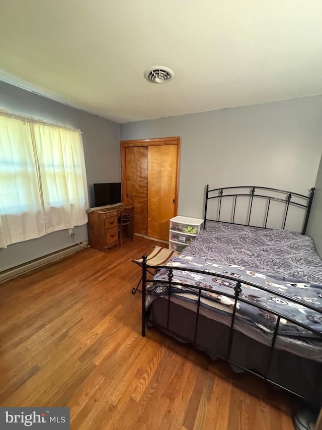 bedroom with light wood-style flooring, a closet, visible vents, and baseboard heating