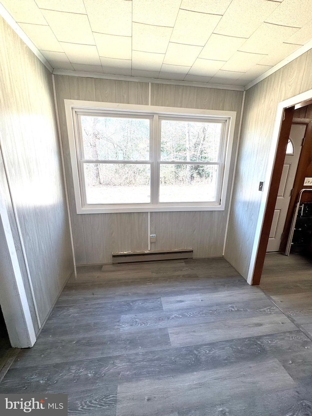 spare room with baseboard heating, crown molding, wooden walls, and wood finished floors