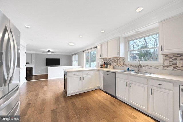 kitchen with a peninsula, a sink, white cabinets, appliances with stainless steel finishes, and light wood-type flooring