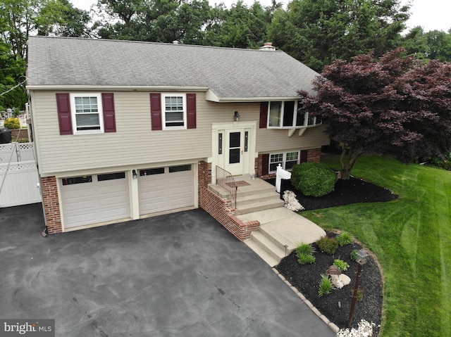 bi-level home with a garage, a shingled roof, aphalt driveway, a front lawn, and brick siding