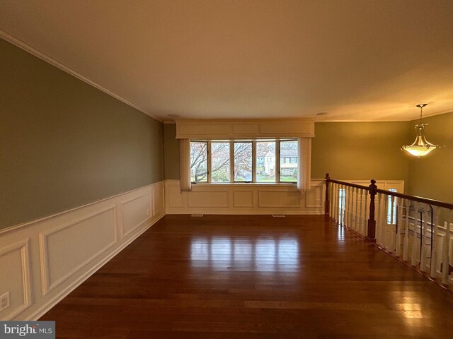 empty room with a wainscoted wall, a decorative wall, dark wood-style flooring, and crown molding