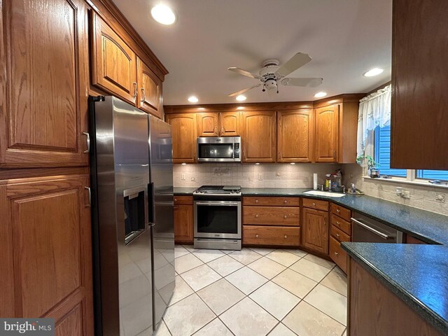 kitchen with light tile patterned floors, stainless steel appliances, dark countertops, backsplash, and brown cabinetry