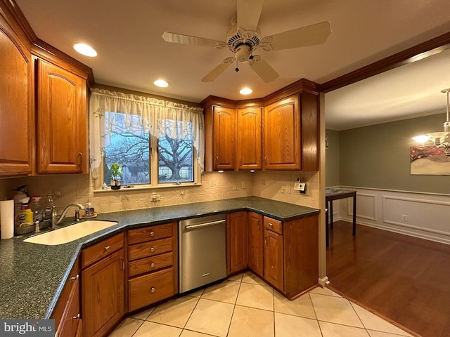 kitchen with light tile patterned floors, a wainscoted wall, a sink, backsplash, and brown cabinets