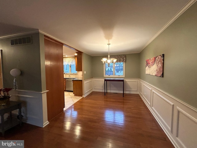 unfurnished dining area featuring visible vents, wood finished floors, crown molding, a chandelier, and a decorative wall