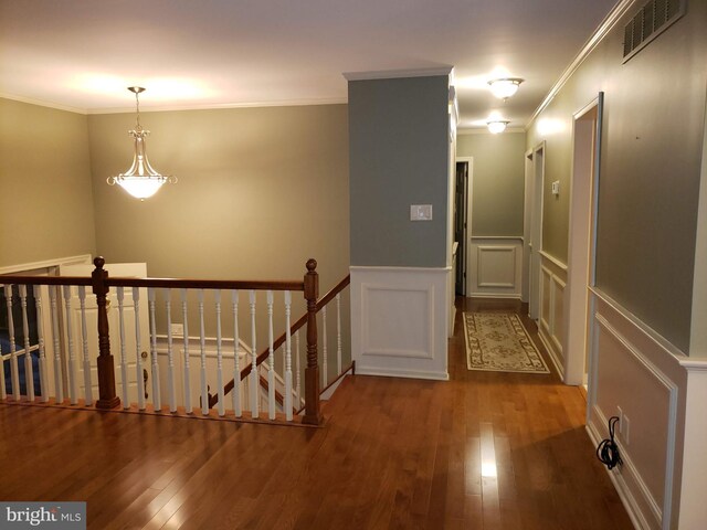 corridor with visible vents, wood finished floors, crown molding, an upstairs landing, and a decorative wall