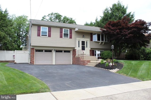 raised ranch featuring driveway, an attached garage, fence, a front lawn, and brick siding