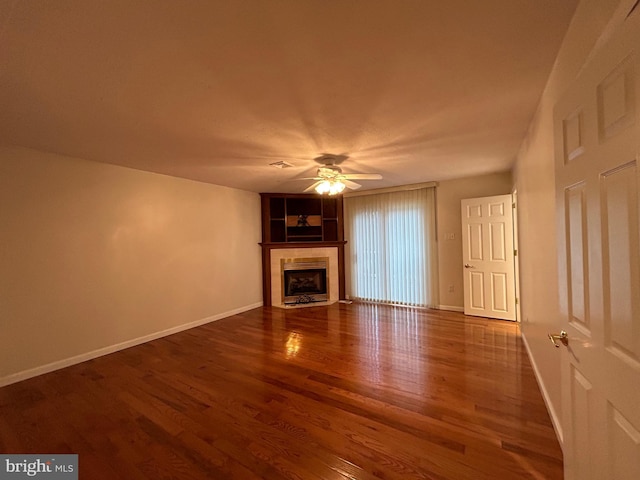 unfurnished living room with baseboards, a ceiling fan, a tiled fireplace, and wood finished floors