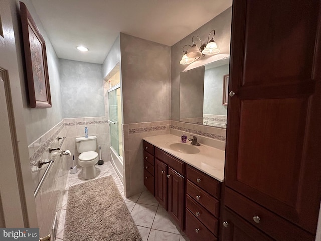 bathroom featuring tile walls, toilet, combined bath / shower with glass door, vanity, and tile patterned flooring