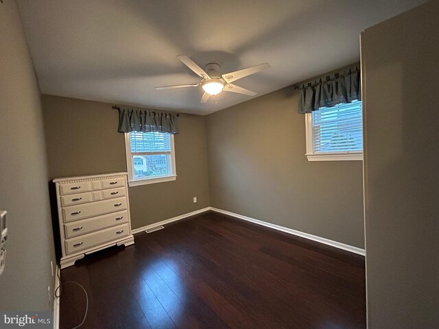 unfurnished bedroom with dark wood-style floors, a ceiling fan, visible vents, and baseboards