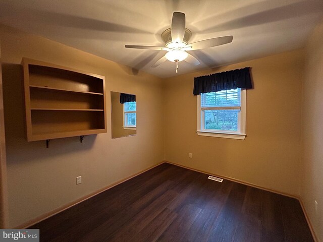 empty room with baseboards, visible vents, a ceiling fan, and dark wood-type flooring