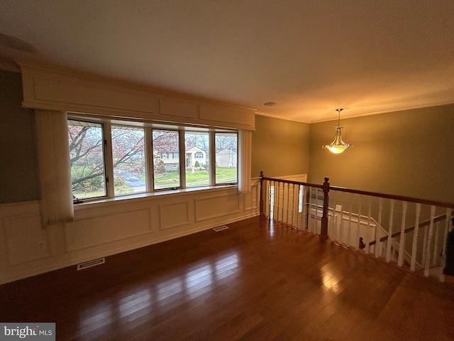 empty room with a decorative wall, dark wood finished floors, visible vents, and crown molding