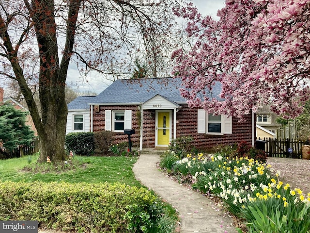 view of front facade featuring brick siding, a shingled roof, a front yard, and fence