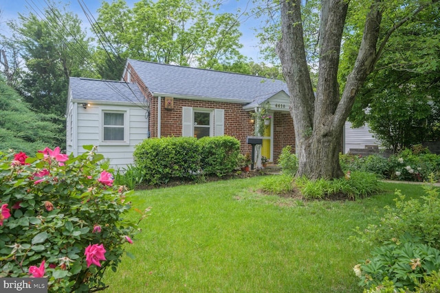 view of front of property with a front yard, brick siding, and roof with shingles