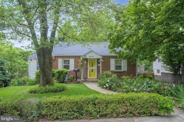 view of front of property featuring brick siding, roof with shingles, and a front yard