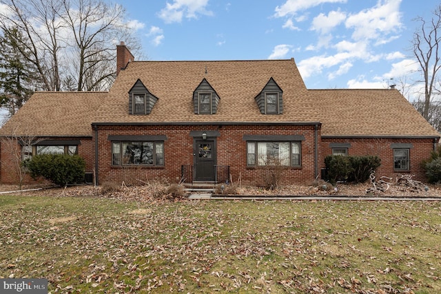 new england style home with a front yard, brick siding, and roof with shingles