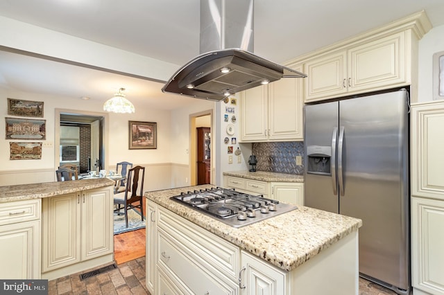 kitchen with light stone counters, island exhaust hood, stainless steel appliances, cream cabinetry, and backsplash