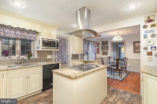 kitchen with backsplash, island exhaust hood, cream cabinets, stainless steel appliances, and a sink