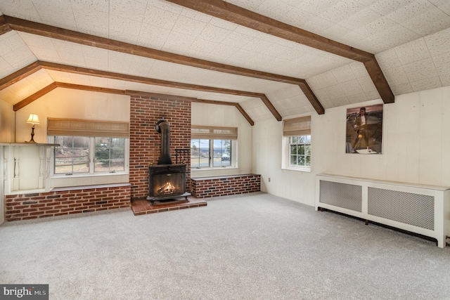 unfurnished living room with radiator, vaulted ceiling with beams, brick wall, carpet flooring, and a wood stove