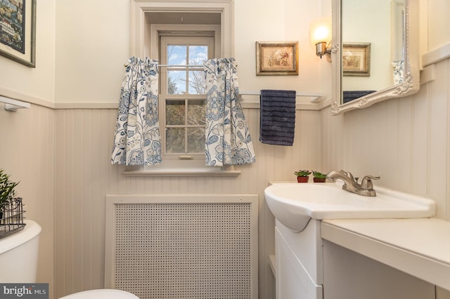 bathroom featuring toilet, radiator heating unit, vanity, and a wainscoted wall